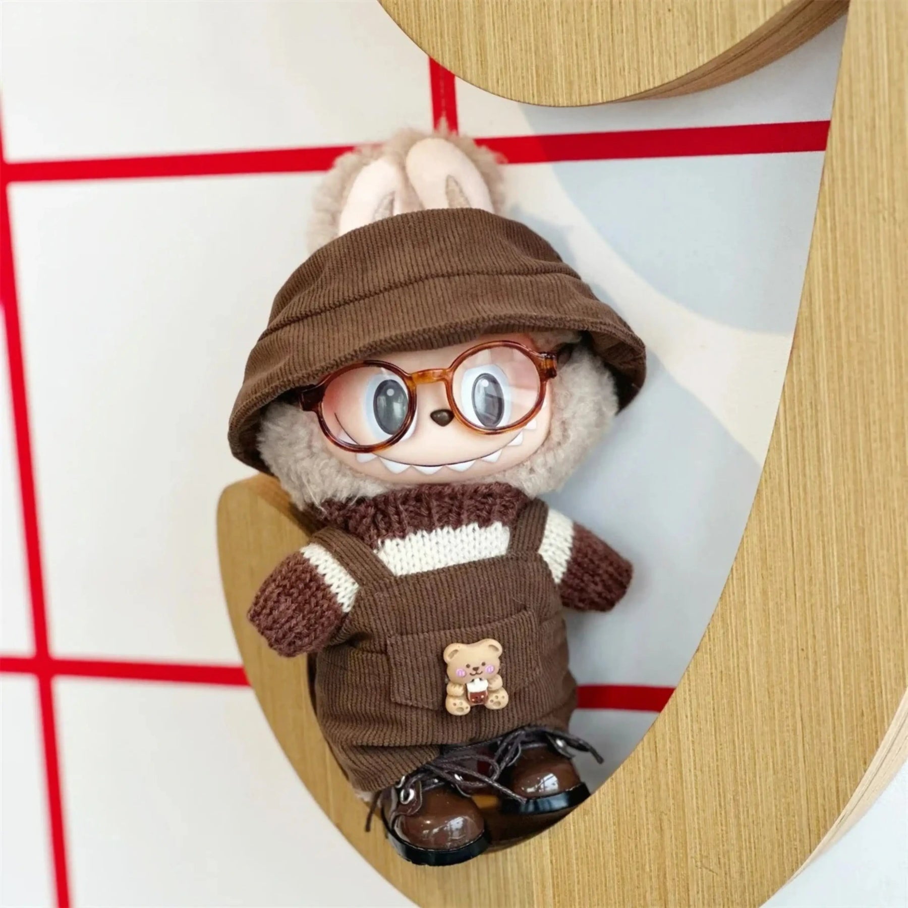 Labubu Popmart com kit marrom de inverno, sentado em cenário decorativo com óculos e jardineira de ursinho